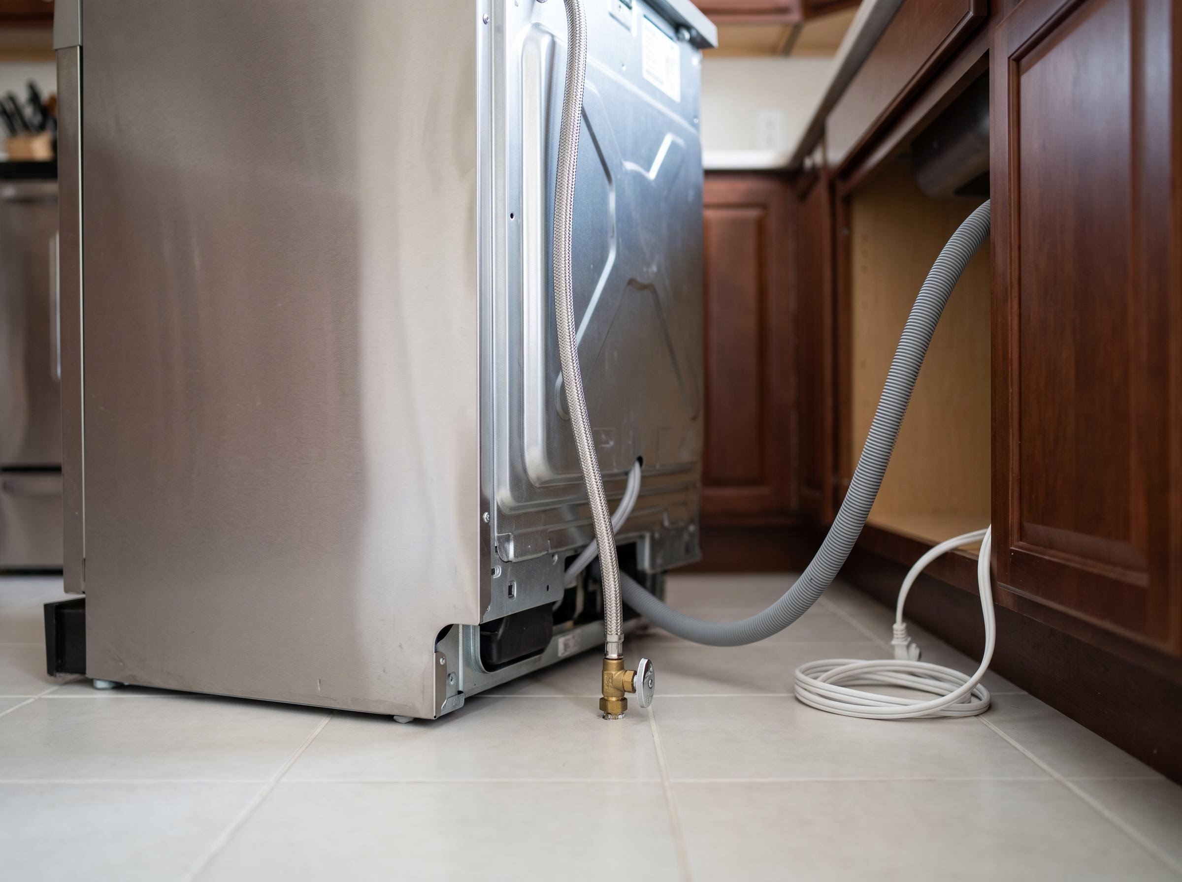 Dishwasher pulled out: water supply, drain hose, and electrical cord at the kickplate.